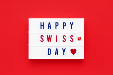 HAPPY SWISS DAY written in a lightbox on a red background. Independence day date. Top view