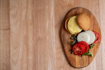 Top view of fresh tasty homemade hamburger with fresh vegetables, lettuce, tomato, cheese beside sliced tomatoes on a cutting board. Free space for text