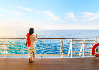 A dark haired woman on enjoys a drink on the deck of a cruise ship passing through the Greek...