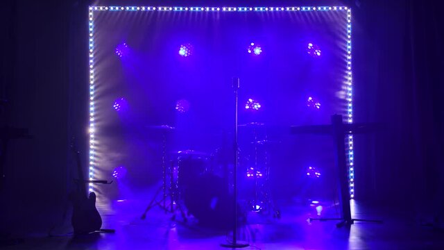 Classic retro chrome microphone and electric guitar together with drums and piano synthesizer keyboard on the stage in dark studio with smoke and neon lighting. Dynamic colored neon lighting effects.