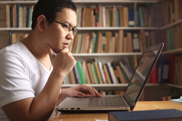 Asian muslim man studying in library, exam preparation concept. Male college student using laptop to learn online