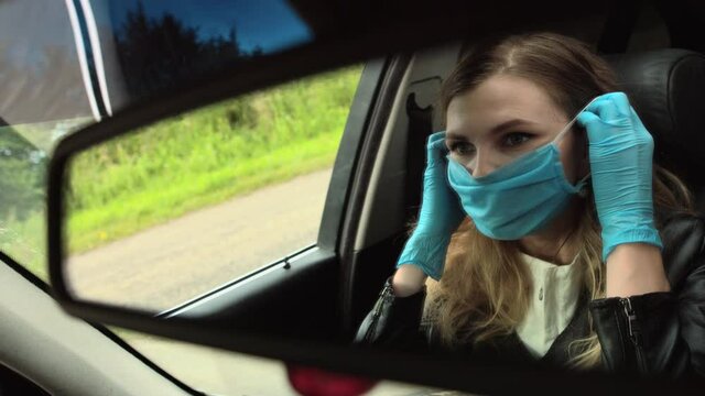 A woman is putting on a medical mask in a car. Coronavirus. Covid -19.view from the car mirror