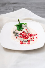 Chile en Nogada, Mexican dish that dates back to the colony, poblano pepper with a cream of walnut, with grains of pomegranate, in a white plate that is on a gray wooden table, next to it is a napkin