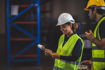 Group of warehouse workers logistic team  wearing hardhats working in aisle between tall racks with...