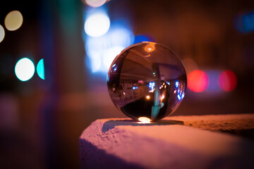 Glass glossy ball in hand against the background of the night neon city, neon light. Night city lights, bokeh light, blurred background.