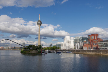 Obraz premium Outdoor sunny view of harbour, pier, pedestrian bridge, Rhein tower and promenade on riverside of Rhein River and cityscape at media harbour, in Düsseldorf, Germany,