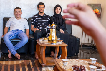 Happy Arabic family sitting together enjoying Arabic coffee and sweets and talking to each other