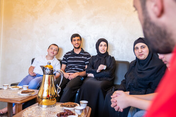 Happy Arabic family sitting together enjoying Arabic coffee and sweets and talking to each other