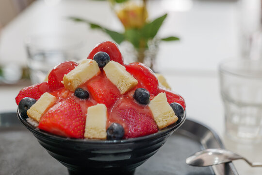 Close up view at Strawberry Patbingsu, Korean shaved ice dessert, served with pieces of cheese and berry topping with background of bright and white cafe.
