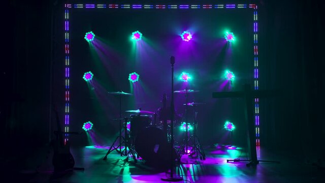 Classic retro chrome microphone and electric guitar together with drums and piano synthesizer keyboard on the stage in dark studio with smoke and neon lighting. Dynamic colored neon lighting effects