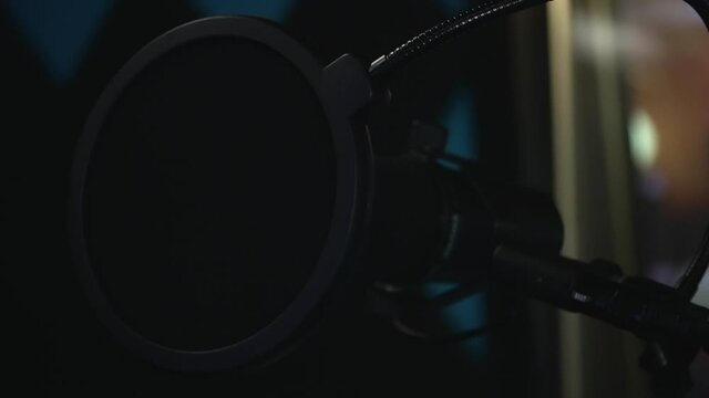 Black studio microphone with a pop filter in recording studio. Panning shot, slow motion, close up