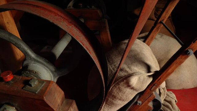 Panning view of vintage grain sacks sitting next to belt pulley of old watermill.