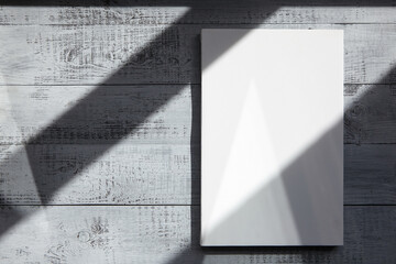 White blank canvas hangs on wooden wall with a shadow from the sunlight covering. Mockup, front view, copy space