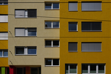 Outdoor sunny exterior front view, typical facade of modern residence or apartment in city of Europe with rectangular windows and various shade of yellow wall.