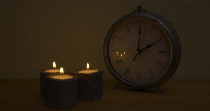 Two o'clock at night, dark scene of wooden table with homey objects, clock telling time, three candles with orange flame, static shot