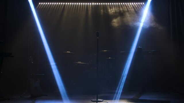 Classic retro chrome microphone and electric guitar together with drums and piano synthesizer keyboard on the stage in dark studio with smoke and neon lighting. Dynamic blue neon lighting effects