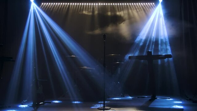 Classic retro chrome microphone and electric guitar together with drums and piano synthesizer keyboard on the stage in dark studio with smoke and neon lighting. Dynamic blue neon lighting effects