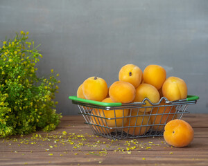 Metal basket with ripe apricots on a plain wooden table close up