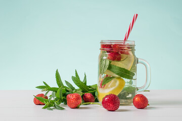 Strawberry berries and mint leaves next to a mug of cold water.