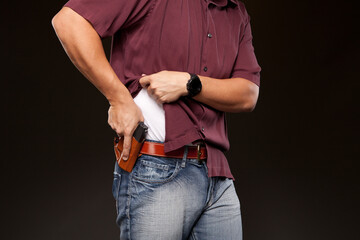 Man lifting up his shirt about to draw his concealed carry pistol from his holster. - obrazy, fototapety, plakaty