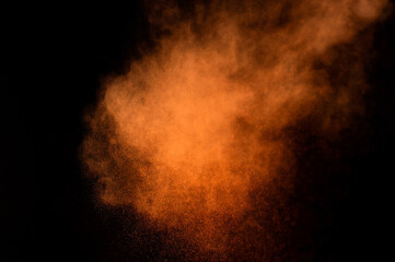 Orange powder explosion on black background. Colored powder cloud. Colorful dust explode. Paint Holi.