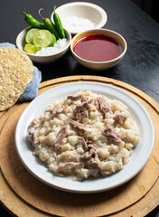 Pozole seco, typical food from colima Mexico accompanied by lemon, onion,  chili, sauce, salt and toasts on a circular plate