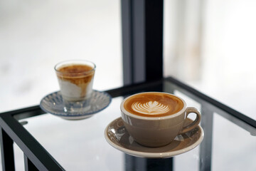 Hot Latte and Dirty Coffee - A cup of coffee with milk and beautiful leaf pattern latte art and A glass of espresso shot mixed with cold fresh milk on blurred background.