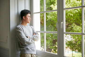 Fototapeta premium young asian man standing by winow at home