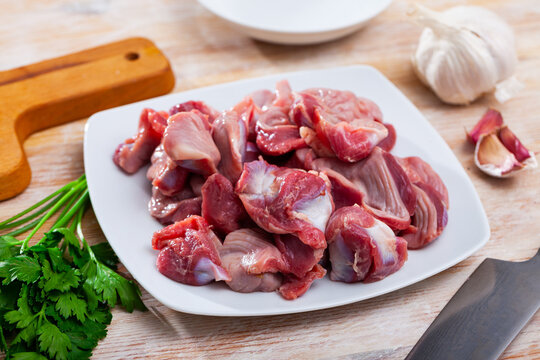 Raw chicken gizzards served on plate on wooden table with herbs and garlic