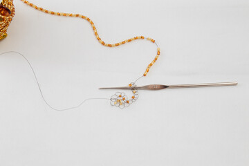 Crochet and black wire with golden or amber colored beads and some loops in process of making handmade jewelry, bijouterie on white fabric background. Workshop, leisure, hobby concept.