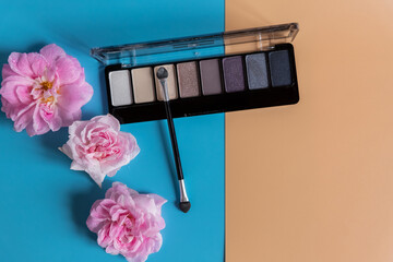 The concept of makeup and office dresscode. palette of shadows with beige, rose, blue and brown shades on colorful background. top view.bright and colorful eye shadows with pink roses buds.Copy space