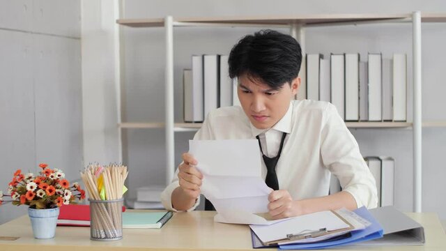 Angry stressed Asian businessman reading bad news in mail letter. Mad man feels frustrated about bad news, dismissal notice, lost job, Depressed jobless person. Unemployment.
