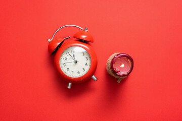 Red alarm clock and burning candle ont he red background.