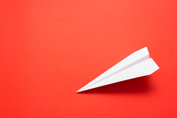 White paper airplane on the red background with copy space.