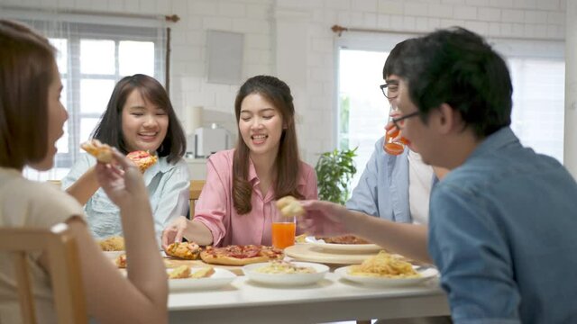 Medium shot happy asian friend eating pizza at home. Group friend cheerful mates laughing enjoying meal having fun sitting together at home dining table, diverse friends share lunch at meeting