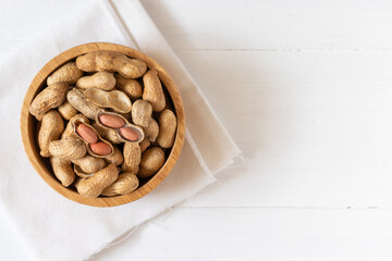 Top view of peanuts in a wooden bowl on white background,