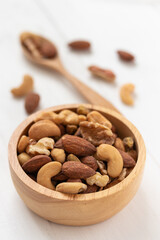 Portrait view of mixed nuts in a wooden bowl on white background