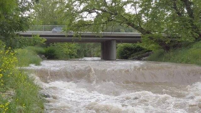 Long sequence of muddy highwater river with a bridge while tilting down in slow motion