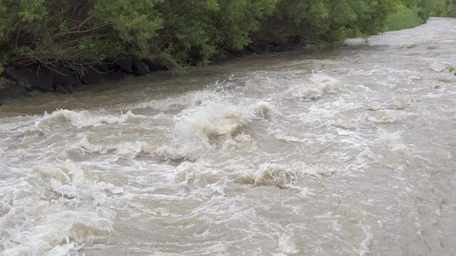 Following the roaring waves of a muddy channelled highwater river in slow motion