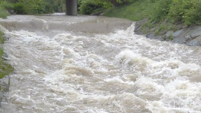 Roaring muddy river with bridge in slow motion, tilting up