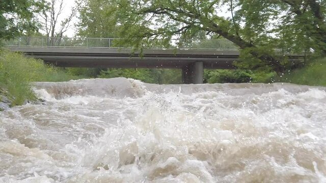 Slow motion splashes of a muddy highwater river with a bridge in Austria