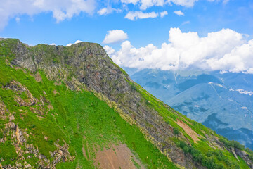 Naklejka premium The top of a rocky mountain on a ridge with green meadows and snow, streams. Aerial drone view, against backdrop of clouds and another mountain range.