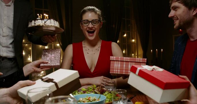 Group of multiethnic friends celebrating birthday. Beautiful caucasian girl is given gifts and blows out candle on special cake - happy people, holidays, friendship concept 4k footage