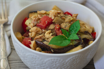 Grilled eggplant salad with fresh tomatoes, walnuts and vinaigrette garnished with basil. Vintage fork in the background 