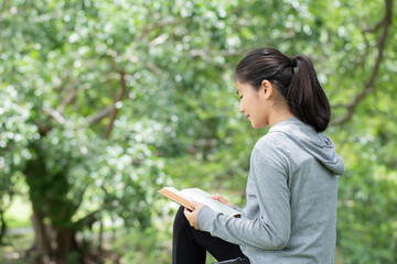 Fototapeta premium Pretty young woman reading bible in park. Reading abook.The concept of God's bible is based on faith and spirituality.