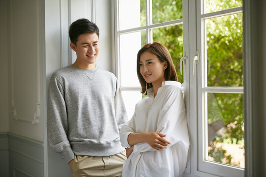 young asian couple staying at home standing by the window talking chatting