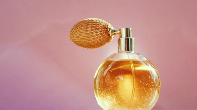 Luxury golden perfume bottle and shining light flares on pink background, glamorous fragrance scent as perfumery product for cosmetic and beauty brand, stock footage