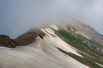 Idyllic summer landscape with hiking trail in the snow mountains and clouds.