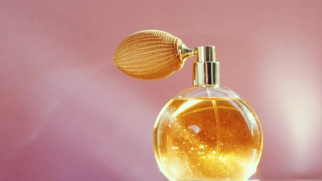 Luxury golden perfume bottle and shining light flares on pink background, glamorous fragrance scent as perfumery product for cosmetic and beauty brand, stock footage
