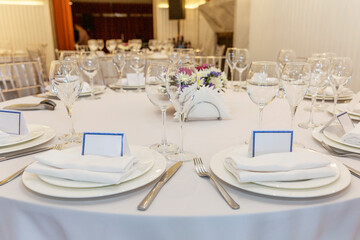 Stylishly served banquet table with personalized cards. Beautiful flowers, empty plates on a white tablecloth. Close-up. Space for text.
